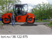 Kamennomostsky, Russia - May 10, 2019: A man with a shovel in his hands is about asphalt compactor roller Hamm. Редакционное фото, фотограф Андрей С / Фотобанк Лори