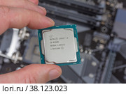 Maykop, Russia - November 9, 2018: man holding fingers intel core I3 desktop processor 8th gen  on background motherboard closeup top view. Редакционное фото, фотограф Андрей С / Фотобанк Лори