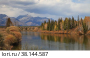 Autumn landscape with yellowed bushes and forest along banks of Irkut River against backdrop of mountain range of Eastern Sayan Mountains on cloudy day in September. Baikal region, Buryatia, Tunka  valley. Стоковое видео, видеограф Виктория Катьянова / Фотобанк Лори