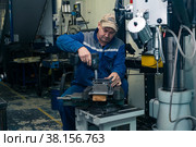Worker in a semi-dark workshop fixes several workpieces in a stack with a power screwdriver (2022 год). Редакционное фото, фотограф Евгений Харитонов / Фотобанк Лори