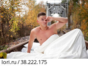 Homeless emotional young athletic beautiful Topless Caucasian man woke up in his bed on railway tracks. Concept of travel ban and inability to move. Stay at home. Copy space for site. Стоковое фото, фотограф Aleksandr Golubev / Фотобанк Лори