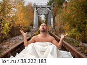 Homeless emotional young athletic beautiful Topless Caucasian man woke up in his bed on railway tracks. Concept of travel ban and inability to move. Stay at home. Copy space for site. Стоковое фото, фотограф Aleksandr Golubev / Фотобанк Лори