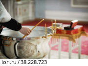 Rite of baptism in an Orthodox Church, priest lights candles at children's baptismal font. Sacrament of Orthodox baptism. Closeup. Стоковое фото, фотограф Aleksandr Golubev / Фотобанк Лори