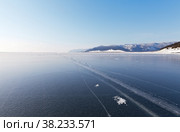 Winter landscape of frozen Lake Baikal. Thin snowless ice with dangerous cracks and snow-covered coastal hills near the village of Bolshoye Goloustnoye on a sunny January day. Natural background. Стоковое фото, фотограф Виктория Катьянова / Фотобанк Лори