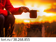 beautiful mature woman brews coffee in a turk in the oven in nature against the backdrop of dawn. Стоковое фото, фотограф Акиньшин Владимир / Фотобанк Лори
