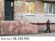 Город Москва, СВАО, улица Академика Комарова, 9а. Женщина вышла из молочно-раздаточного пункта, идет вдоль дома и разговаривает по телефону (2022 год). Редакционное фото, фотограф Наталья Николаева / Фотобанк Лори