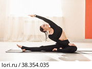 Женщина в черной спортивной одежде практикующая йогу, выполняет упрощенное упражнение паривритта джану ширсасана, тренируется в студии. Стоковое фото, фотограф Сергей Чайко / Фотобанк Лори