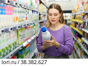 Young positive female customer choosing dairy products in supermarket. Стоковое фото, фотограф Яков Филимонов / Фотобанк Лори