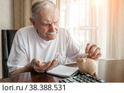 old man in the pandemic counts pennies from the pension fund. Concerned about lockdown, an elderly man puts money in a piggy bank. pensioner calculates the budget of his pension. Стоковое фото, фотограф Оксана Медведева / Фотобанк Лори