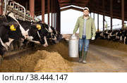 Farmer carrying milk churn near stall with cows in cowshed. Стоковое фото, фотограф Яков Филимонов / Фотобанк Лори