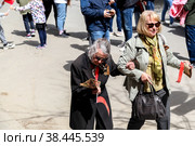 RUSSIA, VOLGOGRAD - May 9, 2022: Two elderly women in glasses with a St. George ribbon on their chests walk down the street on May 9, Victory Day. Volgograd. Редакционное фото, фотограф Владимир Арсентьев / Фотобанк Лори