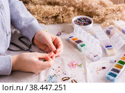 A girl weaves a beaded bracelet on a table among boxes of beads. Сhildren's hobby. Стоковое фото, фотограф Елена Руй / Фотобанк Лори