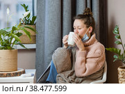 Больная привлекательная молодая женщина простужена и пьет горячий чай, расстроенная молодая блондинка в свитере и одеяле чувствует себя плохо, надевает медицинскую маску. Простуда, высокая температура, грипп, озноб. Стоковое фото, фотограф Photojuli / Фотобанк Лори