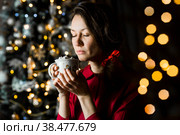 Красивая женщина в красном платье с чашкой кофе и зефиром возле рождественской елки. Красивое боке. Девушка вдыхает аромат напитка. Женщина отдыхает дома на Рождество. Стоковое фото, фотограф Photojuli / Фотобанк Лори