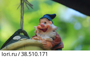 Фигурка садового гнома покачивается на веревочке в саду (2015 год). Редакционное видео, видеограф Цыбин Вадим / Фотобанк Лори