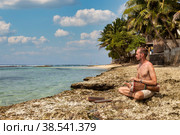 Young man drummer, playing rhythm with djembe drum, sitting on tropical coral reef coast at ocean background. Travel vacation and music relaxation concept. Selective focus. Copy text space. Стоковое фото, фотограф Aleksandr Golubev / Фотобанк Лори