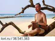 Young man drummer, playing rhythm with djembe drum on tropical sandy beach at ocean background. Travel vacation and music relaxation concept. Selective focus. Copy text space. Стоковое фото, фотограф Aleksandr Golubev / Фотобанк Лори