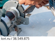 Close-up of men's hands sharpening an axe on an electric sharpener. Repair of home tools with Your own hands. Стоковое фото, фотограф Оксана Медведева / Фотобанк Лори