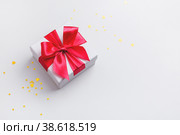 Белая подарочная коробочка с большим красным бантом, на белом фоне с золотистыми блестками. Стоковое фото, фотограф Юлия Трикашная / Фотобанк Лори