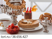 Russian traditions. Russian holiday Maslenitsa. Still life with a cup of tea, a stack of pancakes, sour cream, honey, cubes of butter, bagels, dried fruits, caramel cockerel and samovars. Стоковое фото, фотограф Photojuli / Фотобанк Лори