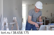Concentrated fifteen-year-old worker checks the house repair plan on a laptop, holding papers with drawings in his hands. Стоковое видео, видеограф Яков Филимонов / Фотобанк Лори