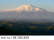 Great nature mountain range. Amazing view of caucasian snow mountain or volcano Elbrus on Bermamyt plateau at sunrise, green fields, blue sky. Elbrus landscape view - highest peak of Russia and Europe. Стоковое фото, фотограф Евгений / Фотобанк Лори