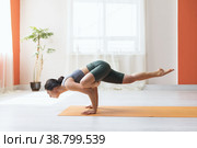 Молодая женщина в коротких леггинсах и футболке, практикующая йогу, выполняет в студии на коврике упражнение эка пада головасана, поза мудреца. Стоковое фото, фотограф Сергей Чайко / Фотобанк Лори
