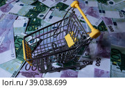 medicines and pills are lying in a small shopping cart against the background of money euro dollars 100 500. pills are poured out of the cart for money the problem of the cost of medicines expensive m. Стоковое фото, фотограф Meshkov Sergey / Фотобанк Лори