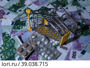 medicines and pills are lying in a small shopping cart against the background of money euro dollars 100 500. pills are poured out of the cart for money the problem of the cost of medicines expensive m. Стоковое фото, фотограф Meshkov Sergey / Фотобанк Лори