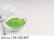 Organic matcha ground powder of green tea leaves served in glass bowl with plant milk and spoon on white wooden background with copy space used as ingredient of healthy latte drink as antioxidant. Стоковое фото, фотограф Елена Кабенкина / Фотобанк Лори