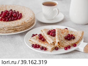 Russian traditions. Russian holiday Maslenitsa. Still life with a cup of tea, a stack of pancakes with northern cranberries, cubes of butter on the table. Стоковое фото, фотограф Photojuli / Фотобанк Лори