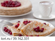 Russian traditions. Russian holiday Maslenitsa. Still life with a cup of tea, a stack of pancakes with northern cranberries, cubes of butter on the table. Стоковое фото, фотограф Photojuli / Фотобанк Лори