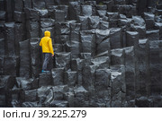 Man wearing yellow coat looking up at Reynisdrangar basalt columns at Reynisfjara Beach, Iceland (2020 год). Стоковое фото, фотограф Igor Tichonow / Фотобанк Лори