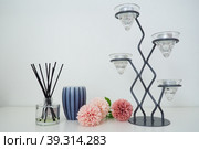 Composition with incense sticks, essential oil in a glass vase and pink terry artificial flowers. Tall metal chandelier with glass holders for small candles. Scented gray striped candle or vase. Стоковое фото, фотограф Юлия Петровская / Фотобанк Лори
