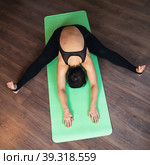 A middle-aged woman leads a healthy lifestyle and practices yoga, performs the exercise Samakonasana, transverse split with a forward bend, trains alone in the studio, sitting on a mat in sportswear. Стоковое фото, фотограф Сергей Чайко / Фотобанк Лори