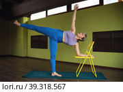 Healthy lifestyle and yoga woman doing Ardha Chandrasana exercise with chair, half moon pose, workout in fitness center in sportswear, full length. Стоковое фото, фотограф Сергей Чайко / Фотобанк Лори