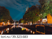 Night shot of Amsterdam canal with illuminated steeples of the church De Krijtberg in downtown Netherlands (2018 год). Стоковое фото, фотограф Igor Tichonow / Фотобанк Лори