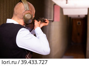 Rear view of man practicing shotgun shooting at target at shooting range. Стоковое фото, фотограф Яков Филимонов / Фотобанк Лори