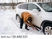 A man digs out a stalled car in the snow with a car shovel. Transport in winter got stuck in a snowdrift after a snowfall, sat on the bottom. First aid, tow truck, winter tires spikes and all-season. Стоковое фото, фотограф Ольга Симонова / Фотобанк Лори