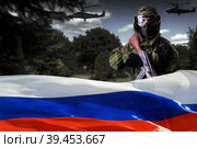 A soldier in camouflage uniform, with a rifle against the background of the flag of Russia and a forest with helicopters, looks into the camera. The concept of guerrilla warfare or the game of airsoft. Стоковое фото, фотограф Владимир Арсентьев / Фотобанк Лори
