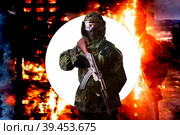 A soldier in camouflage uniform with a rifle against the background of a burning house, looks into the camera. The concept of war or the game of airsoft. Стоковое фото, фотограф Владимир Арсентьев / Фотобанк Лори