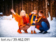 Family including father, mother, little daughter in yellow, red and brown dress on a walk in winter. A man and woman couple and a young girl having play, fun, and walk outdoors in cold time. Стоковое фото, фотограф Кривошеина Елена Леонидовна / Фотобанк Лори