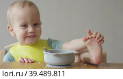 Naughty baby child putting foot leg on table while eating having lunch in kitchen. Стоковое видео, видеограф Olesia Kondrateva / Фотобанк Лори