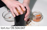 A man grinds dried red peppers in a coffee grinder. Shows the degree of grinding. Grinding hot pepper. Close-up. Стоковое видео, видеограф Vadzim Yakubovich / Фотобанк Лори