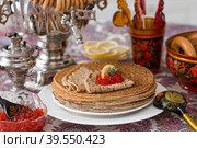 Русские традиции. Русский праздник Масленица. Натюрморт с чашкой чая, стопкой блинов, красной икрой, лимоном, рогаликами, леденцовым петушком, деревянными ложками (хохлома) и самоварами. Стоковое фото, фотограф Photojuli / Фотобанк Лори