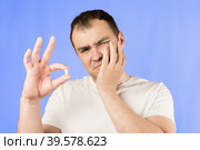 Man in a white T-shirt on a blue background holds a wisdom tooth in his hands after surgical tooth extraction.Man after an operation to remove wisdom teeth.Pain in wisdom teeth, concept of dentistry. Стоковое фото, фотограф Регина Ерофеева / Фотобанк Лори