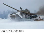 Советский танк Т-54 давит старый легковой автомобиль в заснеженном поле. Танковое шоу в военно-историческом парке "Стальной десант" (2023 год). Редакционное фото, фотограф Виктор Карасев / Фотобанк Лори