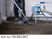 Semi-dry floor screed - a worker shovels a construction mixture through a special sleeve for cementing and leveling on underfloor heating pipes. Стоковое фото, фотограф Ольга Симонова / Фотобанк Лори