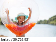 Girl in a hat stands on the river bank with a transparent inflatable circle in the shape of a heart with orange feathers inside. Beach holidays, swimming, tanning, sunscreens. Стоковое фото, фотограф Ольга Симонова / Фотобанк Лори