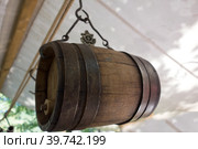 Old wine barrel with iron rings is suspended from a metal hook. Стоковое фото, фотограф Iva Noel / Фотобанк Лори